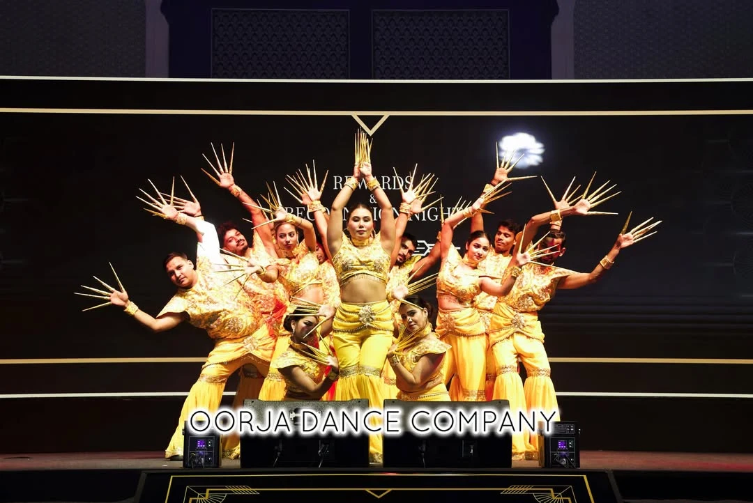 Oorja ensemble in gold costumes forming a many-armed stage composition